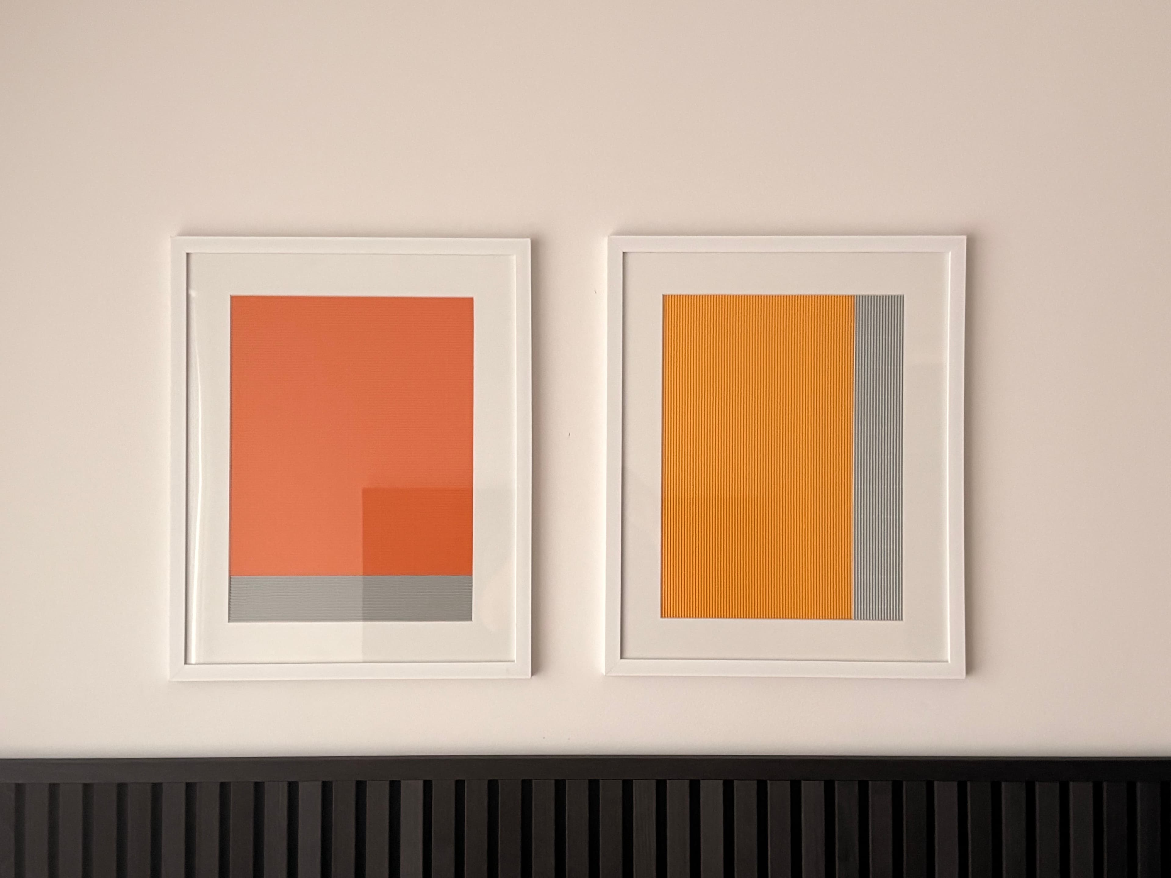 Two white-framed geometric works in orange, yellow and grey, photographed together on a wall.